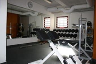 A well-lit indoor gym features weightlifting equipment like dumbbells and benches, creating an energetic atmosphere ideal for fitness enthusiasts seeking strength training facilities.