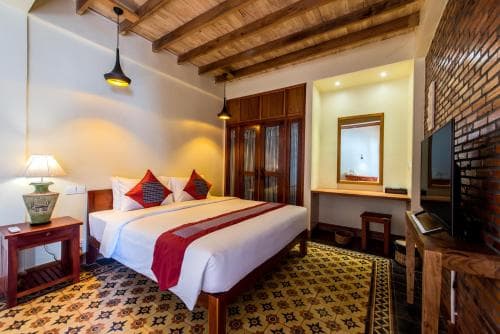 A cozy hotel room with rustic wooden ceilings, brick walls, and patterned carpet exudes warmth, featuring a neatly made bed, vintage decor, and ambient lighting ideal for travelers seeking comfort and charm.