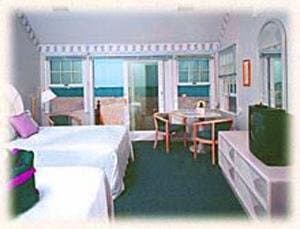 A cozy hotel room with a neatly made bed, wooden furniture, and large windows overlooking greenery, exudes a tranquil atmosphere ideal for a relaxing getaway.