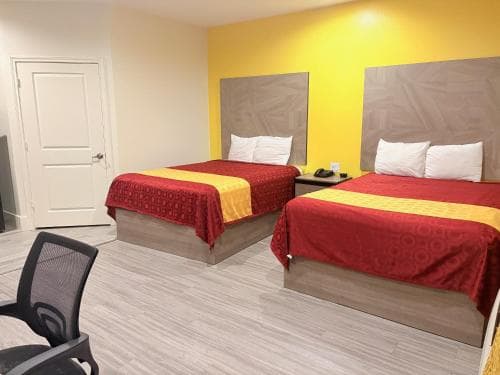 A cozy hotel room features two neatly made beds with red bedding against a vibrant yellow accent wall, creating a welcoming atmosphere ideal for travelers seeking comfort and simplicity.