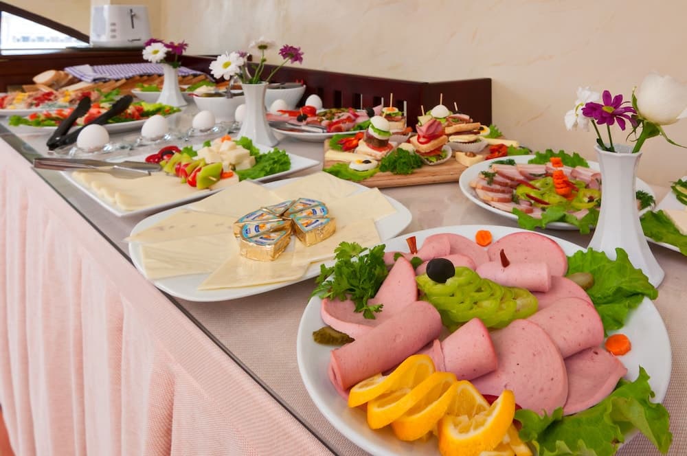 A vibrant buffet table adorned with neatly arranged meats, cheeses, salads, and garnished with fresh flowers creates an inviting atmosphere ideal for a luxurious dining experience at a resort or hotel.