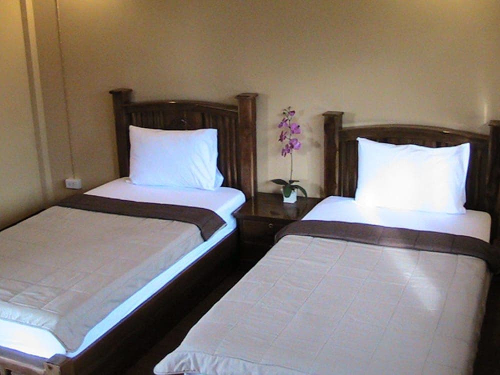 A cozy hotel room features two neatly made twin beds with wooden frames, a small nightstand adorned with a purple orchid, creating a serene atmosphere ideal for travelers seeking comfort and simplicity.