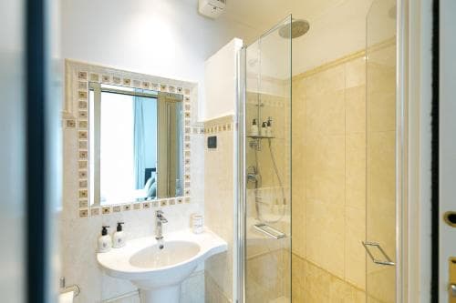 A cozy hotel bathroom features a stylish tiled shower enclosure, a white sink with toiletries, and an ornate mirror, ideal for travelers seeking comfort and cleanliness.