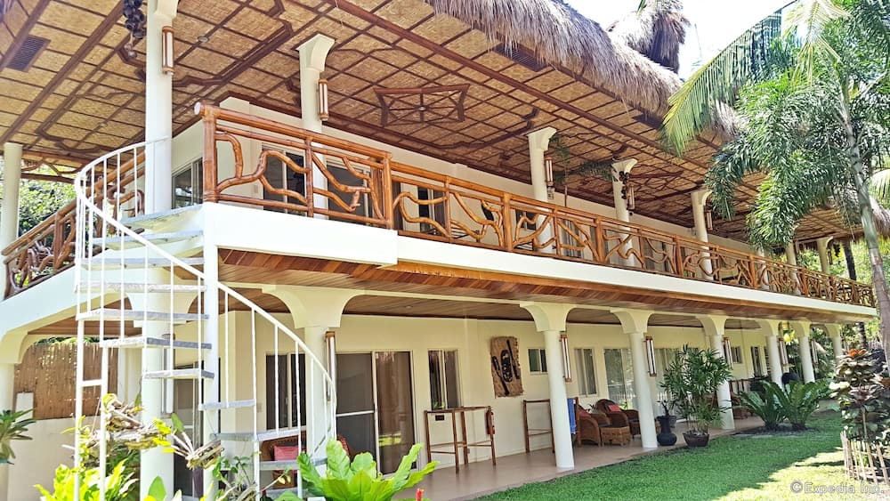 A serene tropical resort features a thatched-roof villa with wooden balconies, lush greenery, and inviting outdoor seating, perfect for a relaxing vacation getaway.