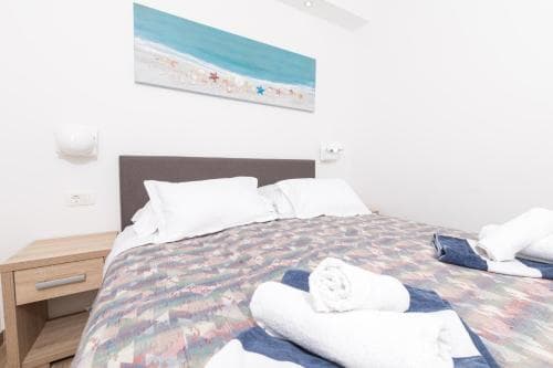 A cozy hotel room features a neatly made bed adorned with colorful bedding, white towels, and a serene beach-themed painting, ideal for travelers seeking relaxation near coastal destinations.