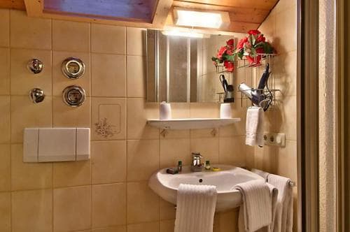 A cozy hotel bathroom features a tiled wall, wooden ceiling, a sink adorned with fresh flowers, and neatly hung towels, ideal for travelers seeking comfort and charm.