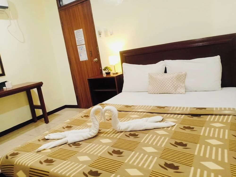 A cozy hotel room features a neatly made bed adorned with patterned bedding and towel swans, complemented by warm lighting, a wooden desk, and a welcoming ambiance ideal for travelers seeking comfort.
