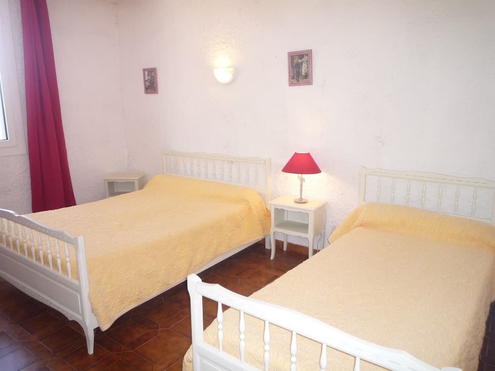 A cozy guesthouse bedroom features two single beds with yellow bedding, white wooden frames, a red lamp on a nightstand, and warm lighting, ideal for travelers seeking a comfortable and inviting stay.