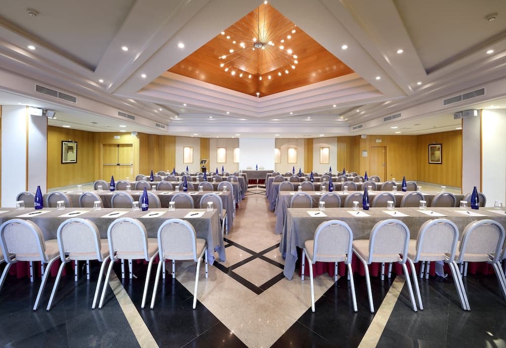 A spacious conference room with elegant wooden ceilings, neatly arranged tables and chairs, and a warm ambiance is ideal for professional meetings and corporate events.