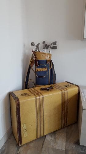 A cozy indoor corner features a vintage yellow suitcase and a golf bag filled with clubs, evoking a nostalgic travel vibe perfect for a golfing getaway or retro-themed trip planning.