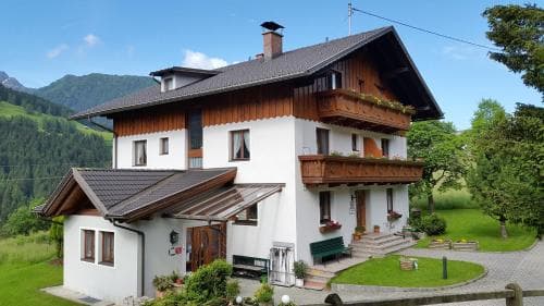 A charming alpine chalet with wooden balconies and lush greenery offers a serene retreat in the mountains, ideal for travelers seeking a peaceful getaway.
