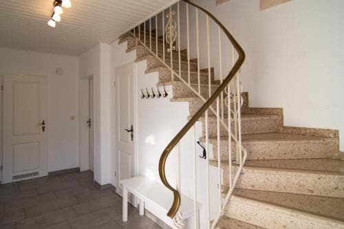 A cozy indoor foyer features a curved staircase with ornate railings, white walls, and a welcoming bench, ideal for travelers seeking a charming and functional entryway in a boutique hotel or vacation rental.