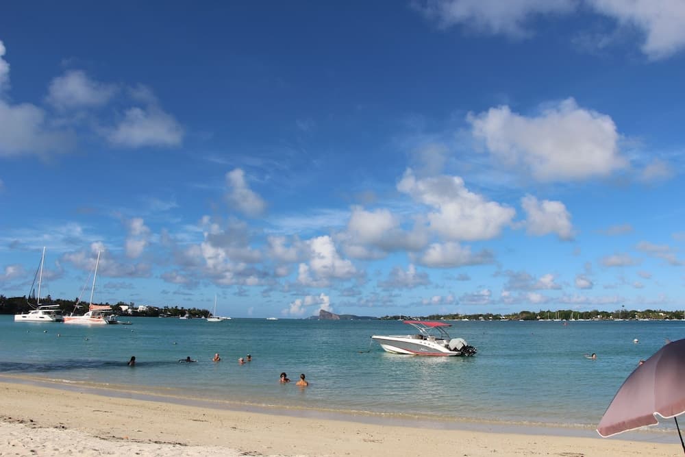 A serene tropical beach scene features clear turquoise waters, scattered boats, and swimmers enjoying the sunny day under a bright blue sky, ideal for vacationers seeking relaxation and water activities.