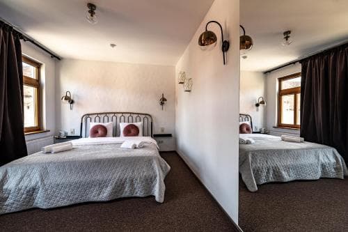 A cozy hotel room with a neatly made bed, warm lighting from wall-mounted lamps, and a window with dark curtains, ideal for travelers seeking comfort and relaxation.