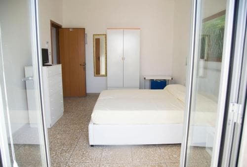 A cozy bedroom with a neatly made bed, mirrored wardrobe, and tiled floor offers a simple yet inviting space for travelers seeking comfortable accommodation.