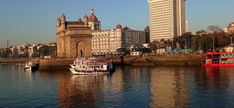 The iconic Gateway of India stands majestically by the waterfront in Colaba, Mumbai, with bustling boats and historic architecture creating a vibrant scene perfect for cultural exploration and photography.