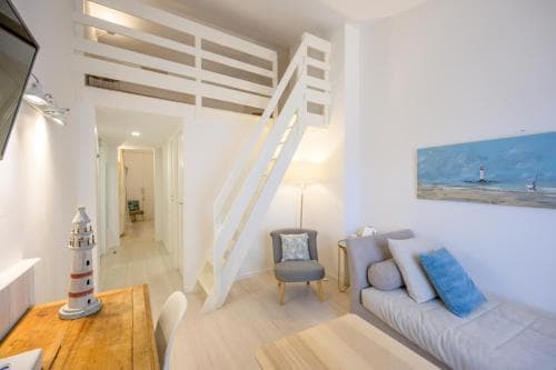 A cozy, nautical-themed apartment features a loft bed, lighthouse decor, and serene artwork, creating an inviting atmosphere ideal for a relaxing seaside getaway.