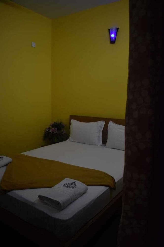 A cozy hotel room with vibrant yellow walls, a neatly made bed adorned with folded towels, and a soft purple wall light creates an inviting atmosphere perfect for travelers seeking comfort and relaxation.