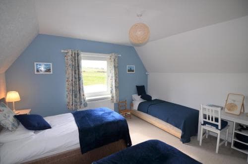 A cozy attic bedroom with slanted ceilings, blue bedding, and a window view of greenery, ideal for a peaceful retreat or family vacation accommodation.