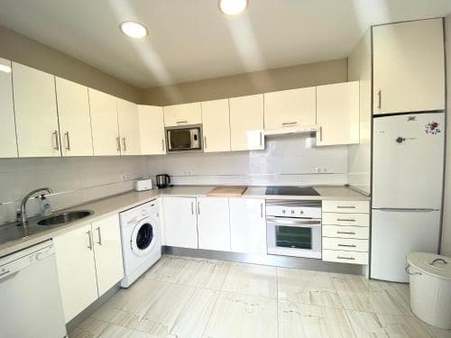 A modern, well-lit kitchen with white cabinetry, stainless steel appliances, and a tiled floor creates a clean and functional space ideal for travelers seeking self-catering accommodations.