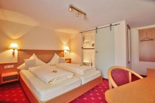 A cozy hotel room features a neatly made double bed with white linens, warm lighting from bedside lamps, a red carpeted floor, and a sliding barn door leading to a bathroom, ideal for travelers seeking comfort and convenience.