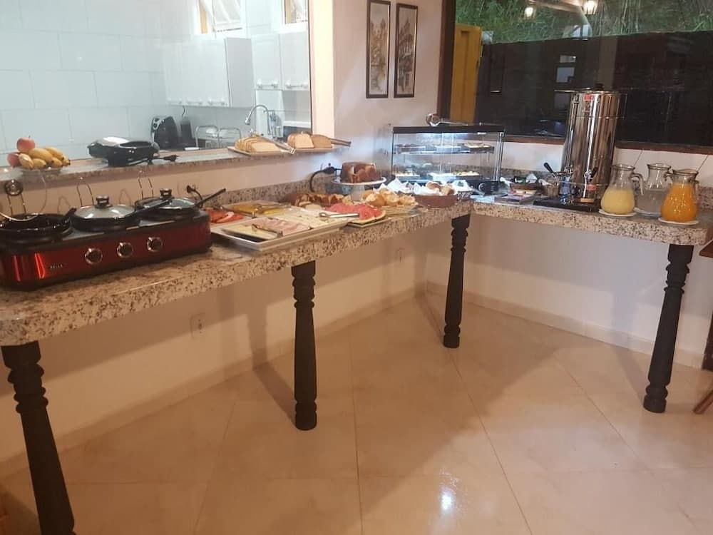 A cozy indoor buffet area with a granite countertop laden with fresh fruits, breads, and beverages, set against tiled floors and framed artwork, ideal for travelers seeking a comfortable dining experience in a relaxed setting.