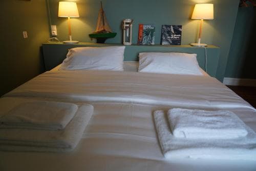 A cozy hotel room features a neatly made bed with white linens, folded towels, bedside lamps, and decorative items like books and a model sailboat, ideal for travelers seeking comfort and relaxation.