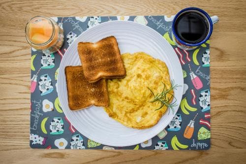 A cozy breakfast scene featuring scrambled eggs, toast, and beverages on a colorful placemat atop a wooden table, perfect for a relaxing morning or a culinary blog post.