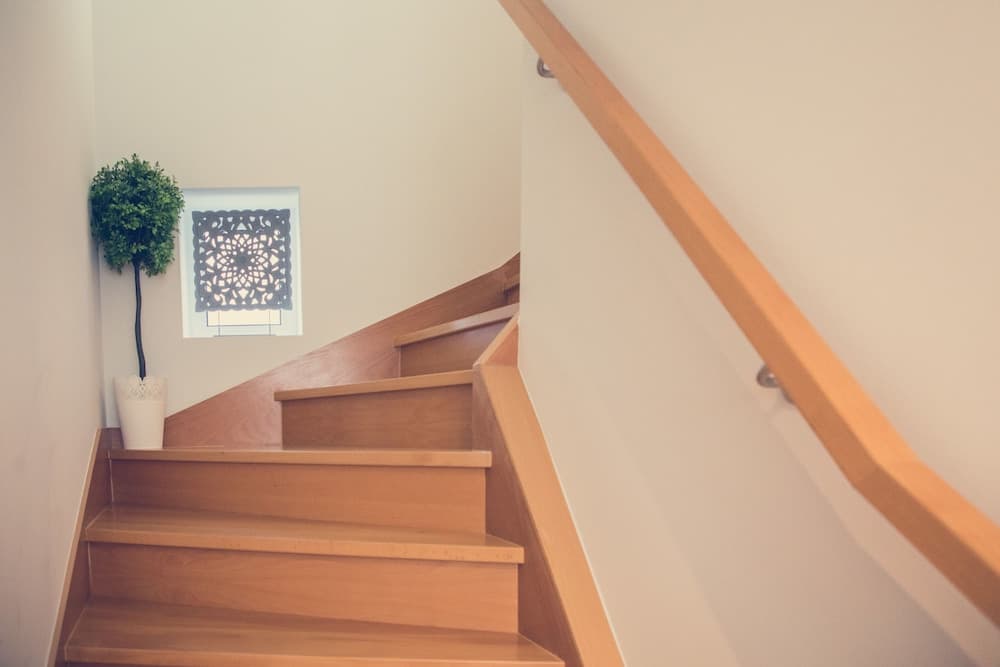 A serene indoor staircase with wooden steps, a sleek railing, and a decorative wall piece accompanied by a potted plant creates an inviting atmosphere ideal for home interior design inspiration.