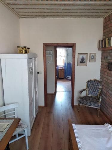 A cozy guesthouse room features wooden floors, vintage furniture, and a view through an open doorway into a bathroom, ideal for travelers seeking a quaint and comfortable stay.