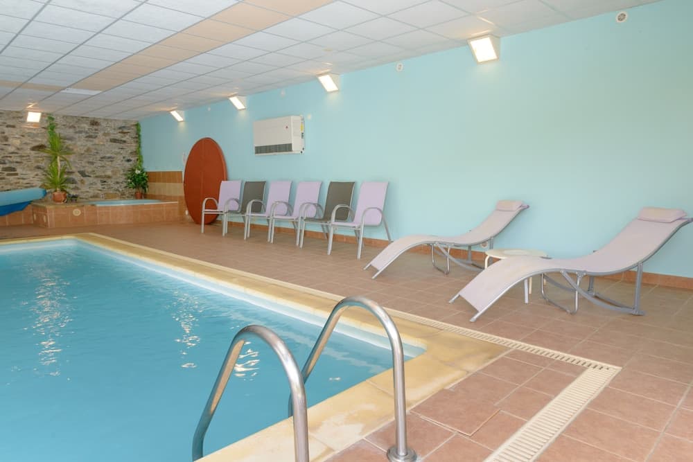 A serene indoor pool area features clear blue water, lounge chairs, and a tiled deck, ideal for relaxation and leisure in a tranquil resort setting.