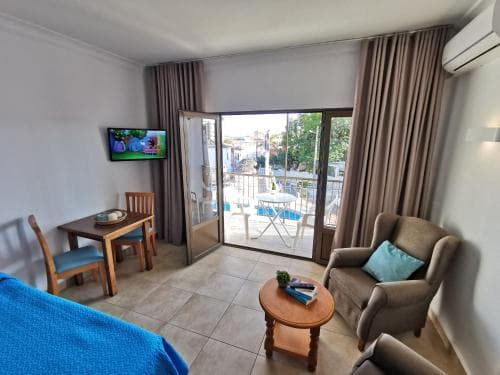 A cozy hotel room with a tiled floor, wooden furniture, and a balcony overlooking a serene outdoor area, ideal for travelers seeking comfort and relaxation.