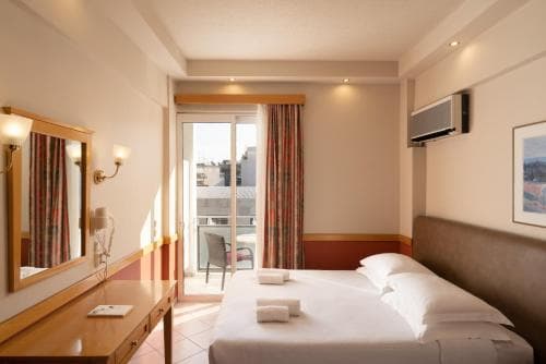 A cozy hotel room with a neatly made bed, wooden furnishings, and a balcony view, exudes warmth and comfort, ideal for travelers seeking relaxation during their stay.
