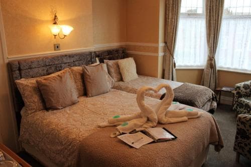 A cozy hotel room features a warmly lit bed adorned with swan-shaped towels forming a heart, evoking a romantic atmosphere ideal for a couples' getaway.