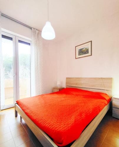 A cozy bedroom with a vibrant red bedspread, wooden furniture, and a framed picture exudes warmth, ideal for travelers seeking a comfortable stay in a serene indoor retreat.