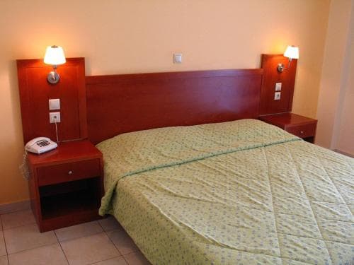 A cozy hotel room features a neatly made bed with a green patterned duvet, wooden bedside tables with lamps, and a warm ambiance ideal for travelers seeking comfort and relaxation.