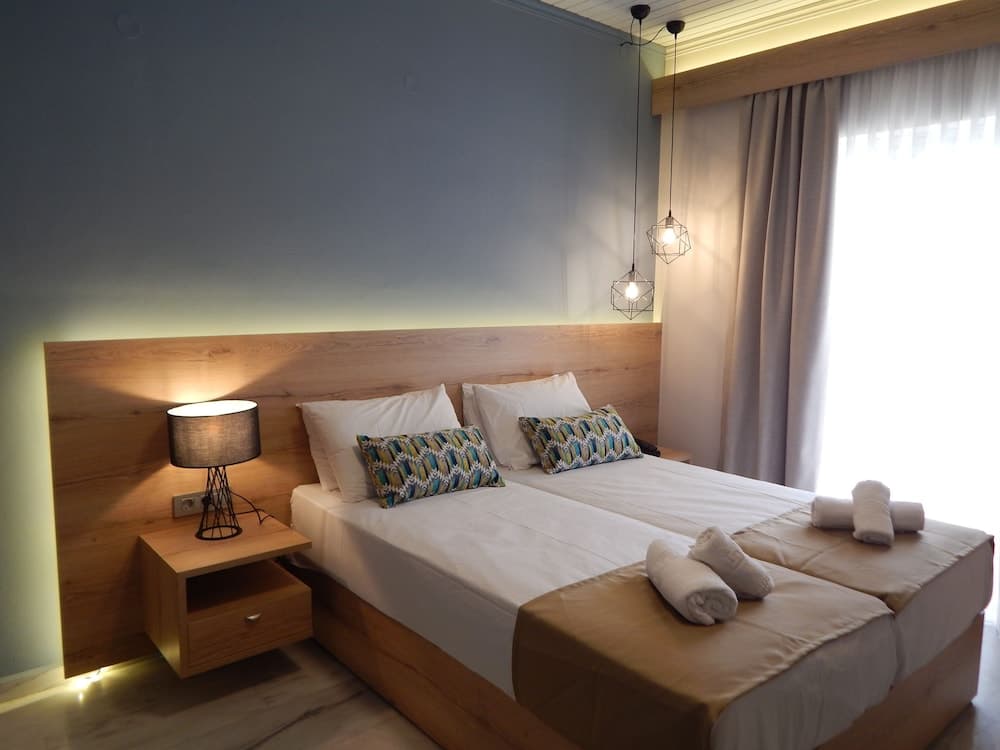A cozy hotel bedroom features a neatly made bed with patterned pillows, wooden furnishings, geometric pendant lights, and soft lighting, ideal for travelers seeking comfort and relaxation.
