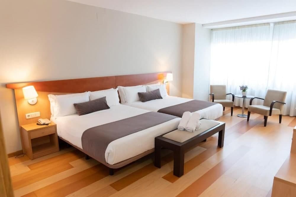 A cozy hotel room with two neatly arranged beds, soft lighting, and a seating area by the window offers a comfortable retreat for travelers seeking relaxation.
