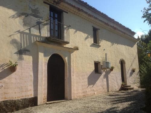 A rustic stone building with arched doorways and balconies bathed in sunlight creates a serene countryside atmosphere, ideal for travelers seeking a tranquil retreat in a historic setting.