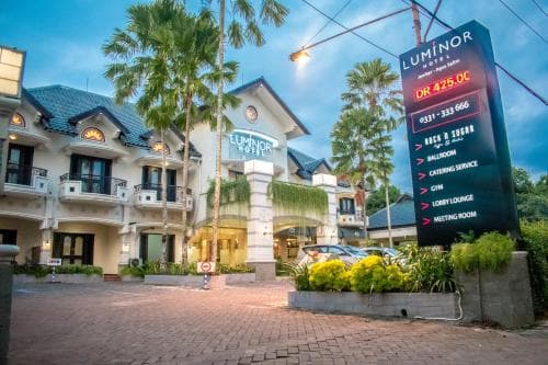 A vibrant evening scene at a tropical hotel entrance, featuring palm trees, a digital sign listing amenities like a gym and meeting room, and a cozy ambiance ideal for travelers seeking relaxation and business conveniences.