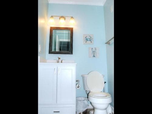 A cozy bathroom with light blue walls, framed mirror, and nautical-themed decor offers a serene retreat for travelers seeking comfort during their stay.