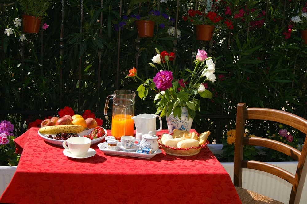 A vibrant outdoor breakfast setup on a patio features a red tablecloth, fresh fruits, pastries, and flowers, creating an inviting and serene morning ambiance ideal for leisurely dining experiences.