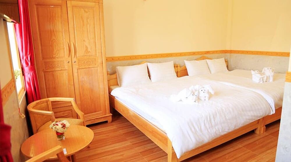 A cozy hotel room with warm yellow walls, wooden furniture, neatly arranged white bedding adorned with towel animals, and a small table with flowers, ideal for travelers seeking comfort and relaxation.