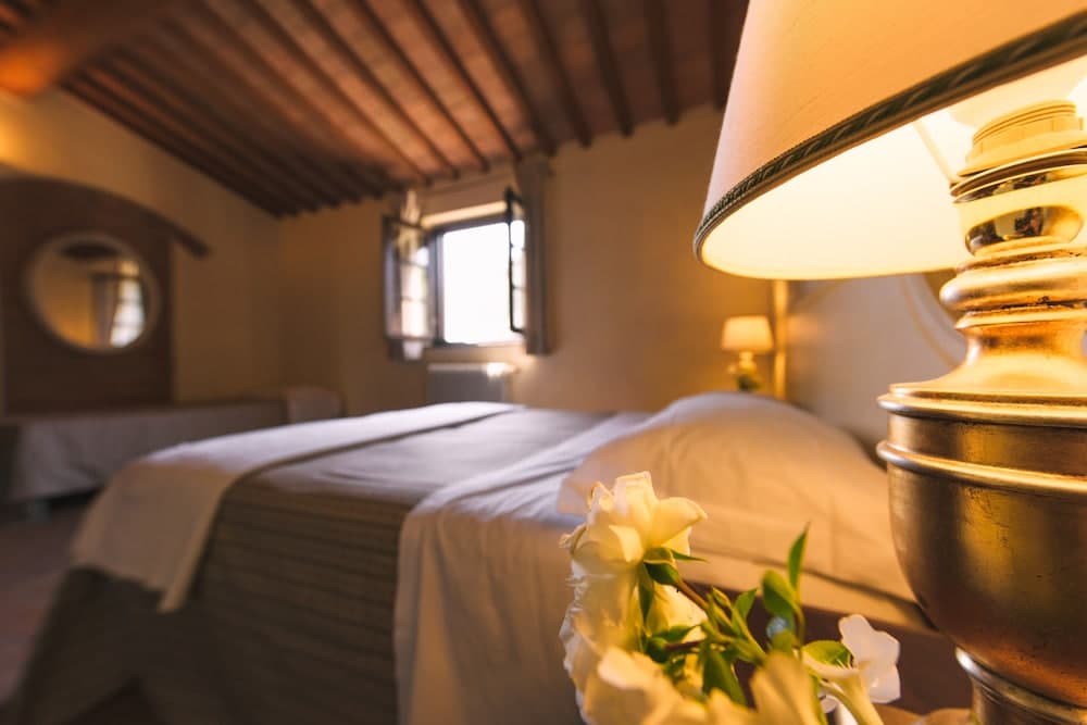 A cozy bedroom with rustic wooden beams, soft lighting from a brass lamp, white roses on the bedside table, and a serene ambiance ideal for a relaxing getaway.