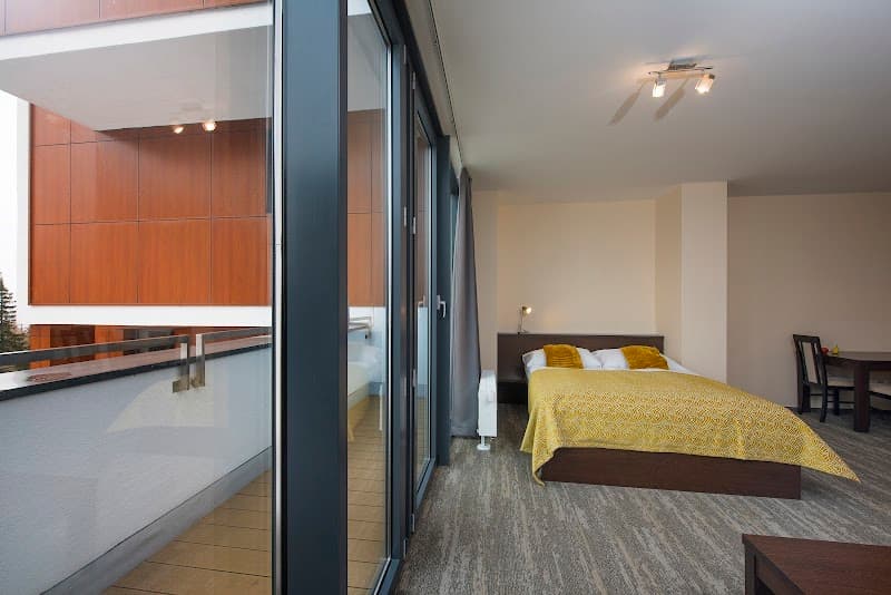A cozy hotel room at the Hotel Panorama Resort in Štrbské Pleso, Slovakia, features a warm yellow bedspread, modern furnishings, and a serene balcony view, ideal for travelers seeking relaxation and comfort in the High Tatras.