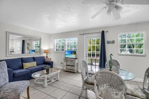 A cozy living room with a blue sofa, wicker furniture, and large windows overlooking greenery, ideal for a relaxing vacation rental experience.