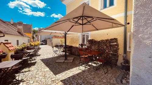 A charming cobblestone courtyard lined with rustic tables under a large umbrella, evoking a cozy European café vibe perfect for travelers seeking a quaint outdoor dining experience.