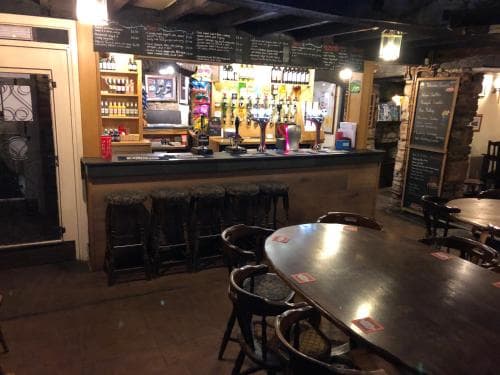 A cozy pub interior with wooden tables, stools, and a well-stocked bar exudes warmth and charm, ideal for travelers seeking a relaxing evening drink and social atmosphere.