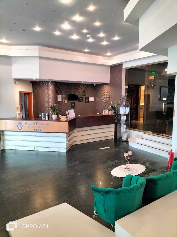 A modern hotel lobby features sleek reception desks, plush green armchairs, and a polished floor, creating a welcoming atmosphere ideal for travelers seeking comfort and convenience.