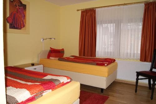 A cozy hotel room with two neatly arranged beds, warm yellow walls, red curtains, and a vibrant artwork creates an inviting atmosphere ideal for travelers seeking comfort and relaxation.